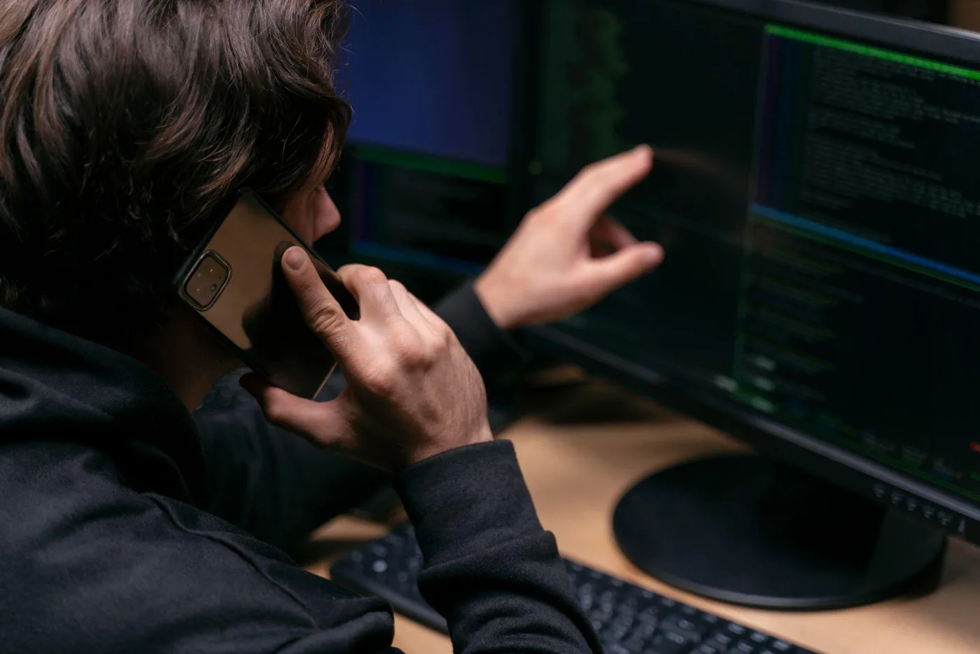 Cybersecurity analyst working at computer screens while communicating by phone